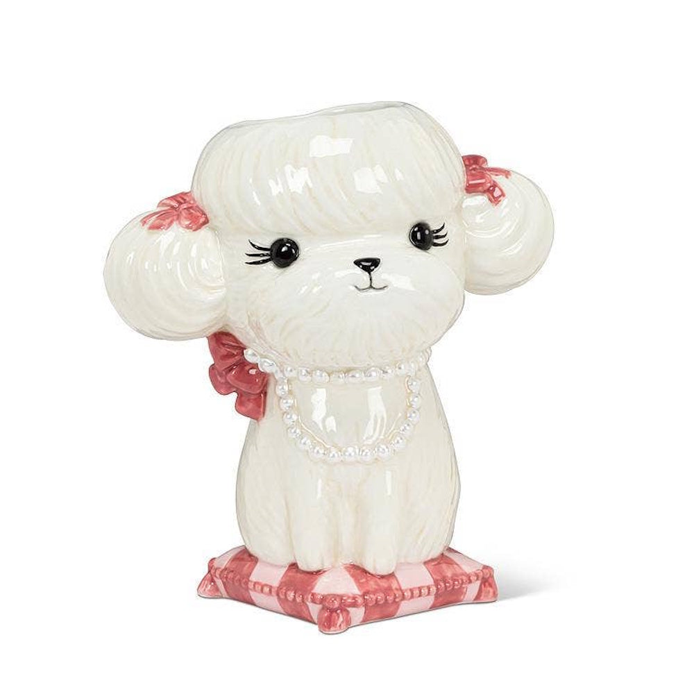 White ceramic poodle vase wearing a pearl necklace, sitting on a pink patterned cushion.