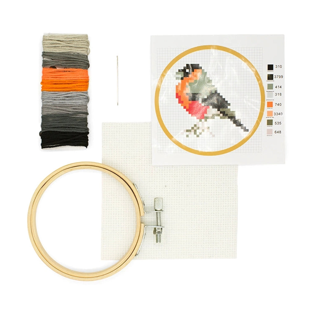 Mini bird cross-stitch kit with embroidery hoop, colorful thread, needle, fabric, and pixelated bird pattern.