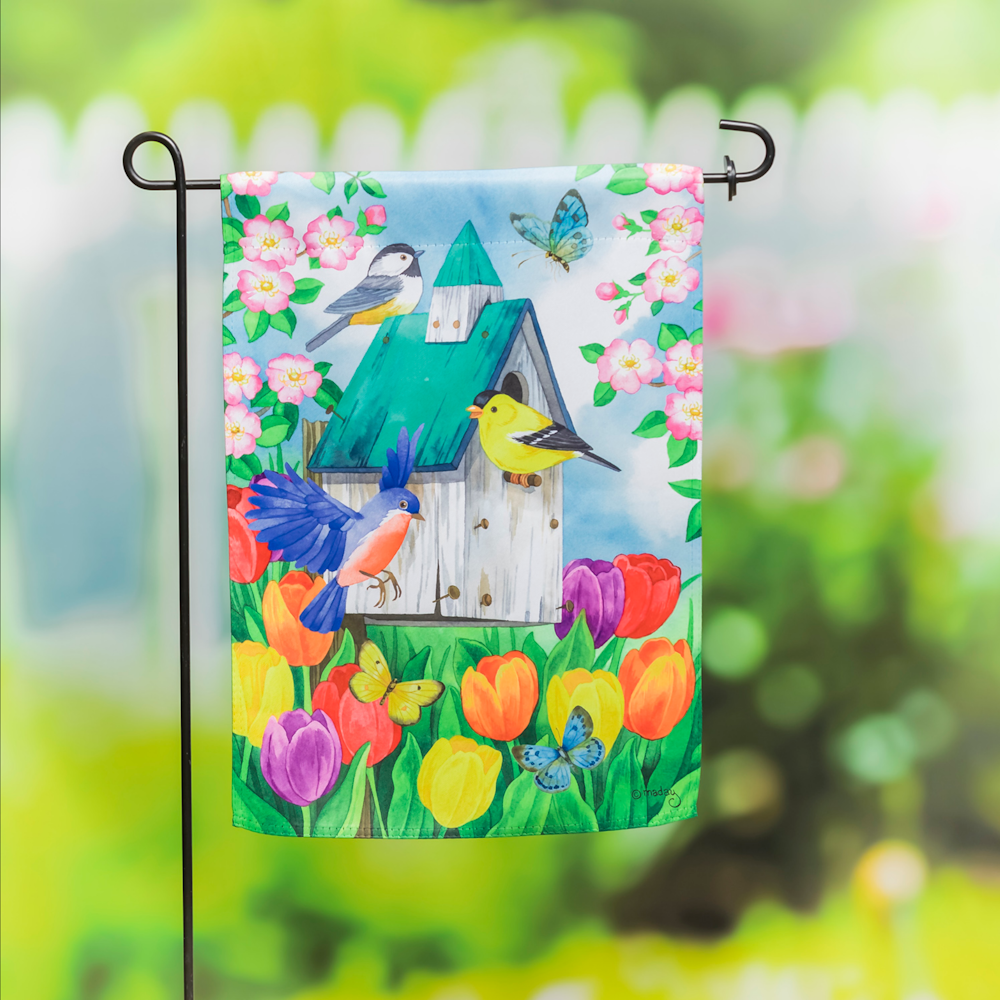 A decorative garden flag featuring a colorful birdhouse surrounded by vibrant tulips, birds, and butterflies.