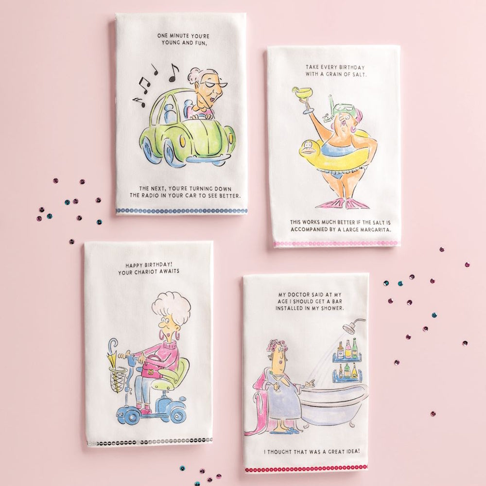Four white hand towels with funny birthday cartoons and sequins, arranged on a pink background.