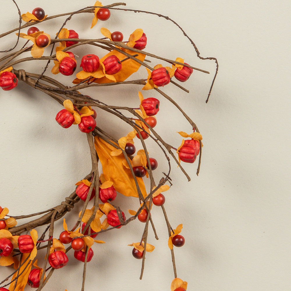 Close-up view of an autumn berry candle ring featuring red berries, orange husks, and brown twigs.