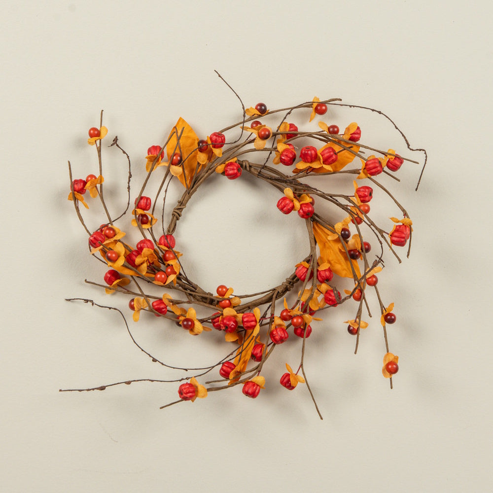Bittersweet berry and orange leaf autumn candle ring made of natural twig branches on a plain background.