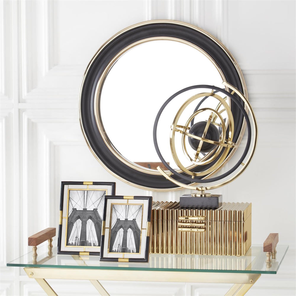 Elegant home decor display with a round black and gold mirror, armillary sphere, and gold fluted jewelry box.