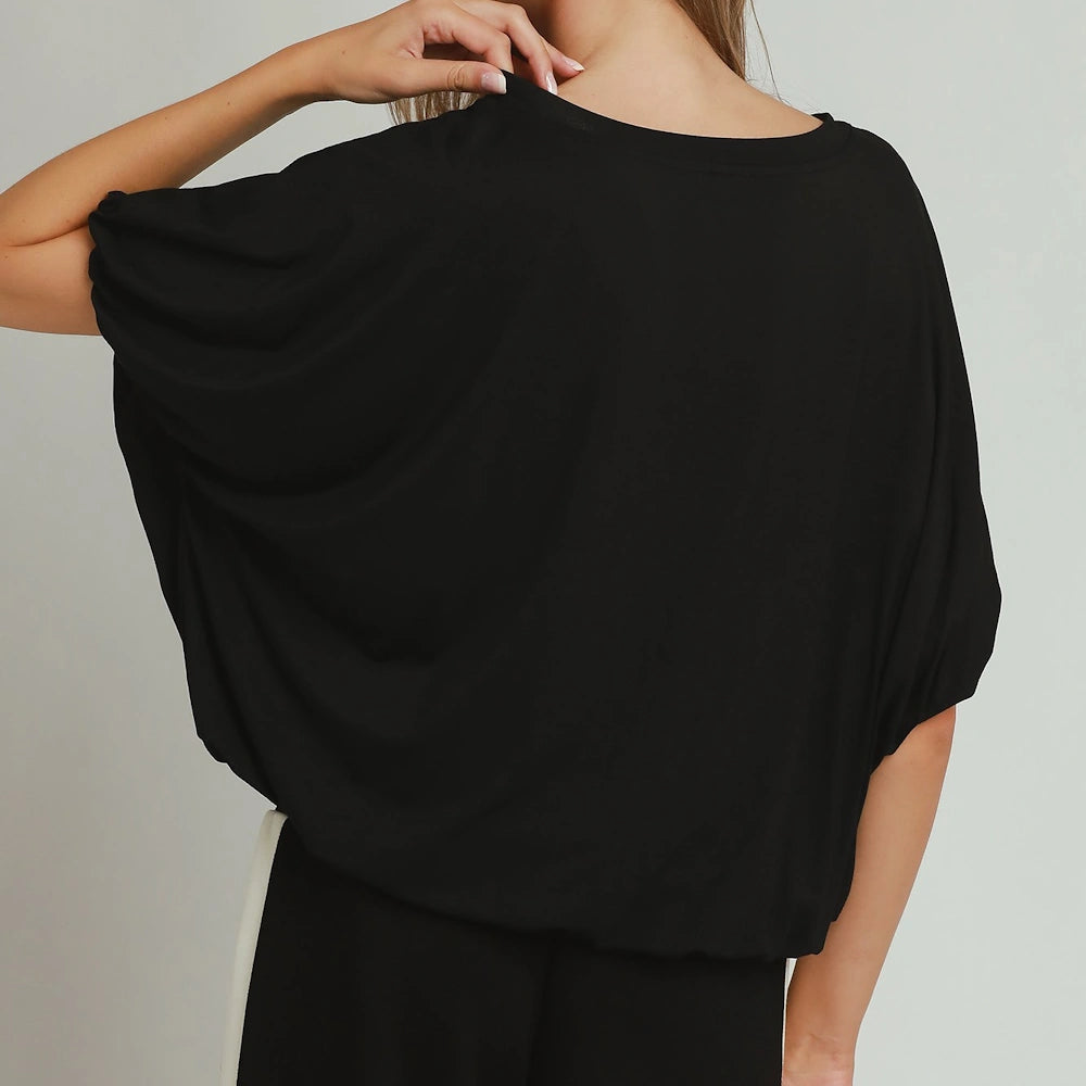 Woman wearing a black draped top with batwing sleeves and a bubble hem, back view.