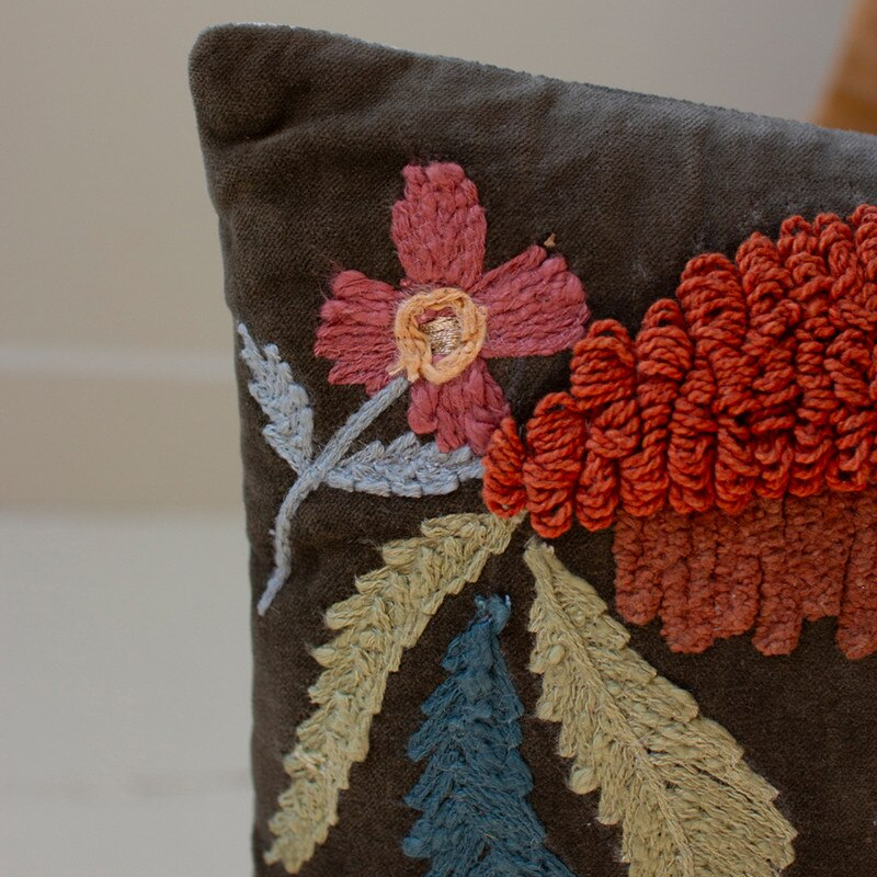 Close-up of a dark grey pillow with colorful textured floral embroidery and leaves.