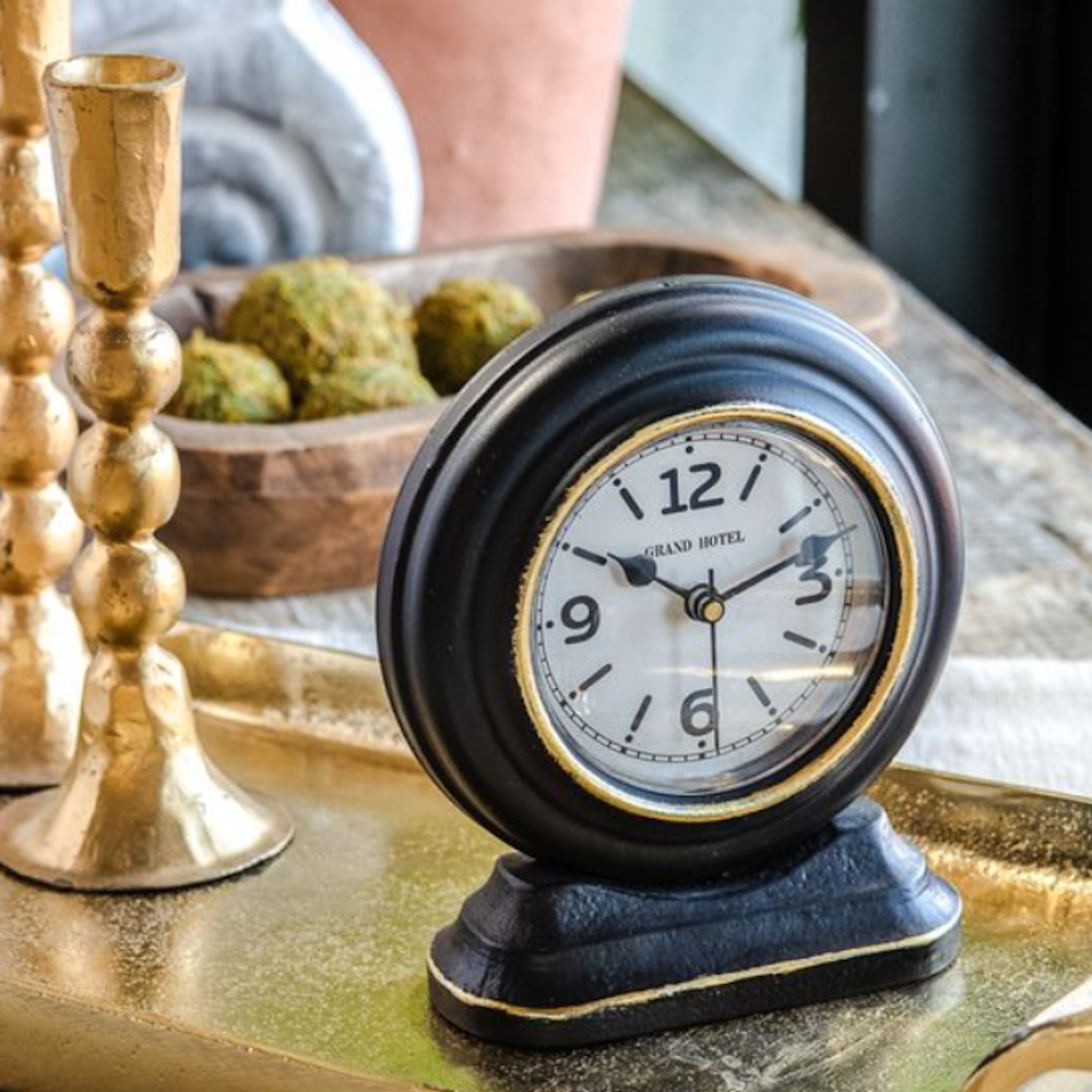 Vintage-style round black table clock with gold trim and a white face reading Grand Hotel.