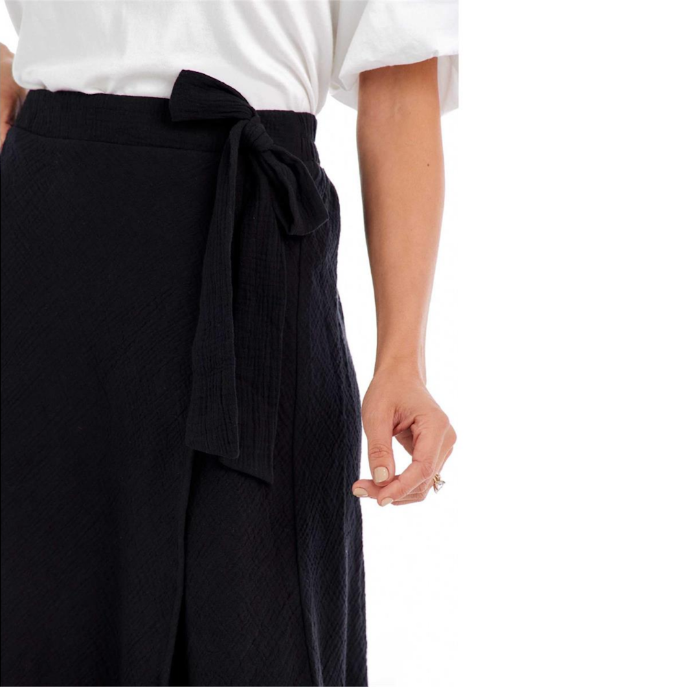Close-up of a person wearing a black textured wrap skirt featuring a side tie bow at the waist.