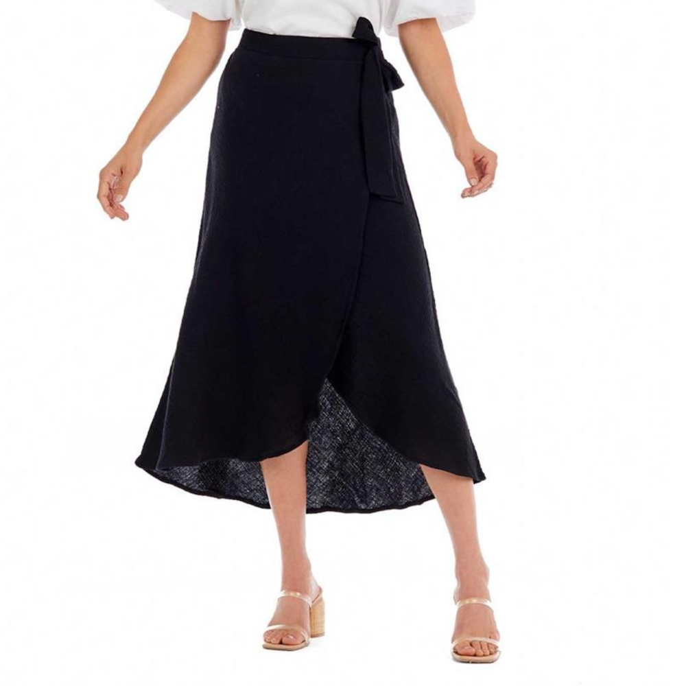 A woman wearing a black wrap skirt tied at the waist with an asymmetrical hemline and neutral heels.