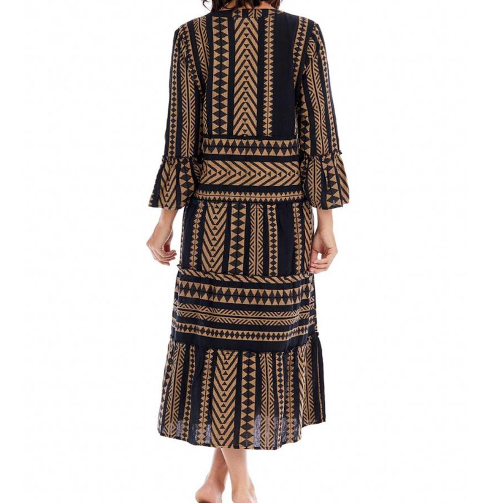 Back view of a woman wearing a black midi dress featuring a tan geometric, tribal print and tiered skirt.