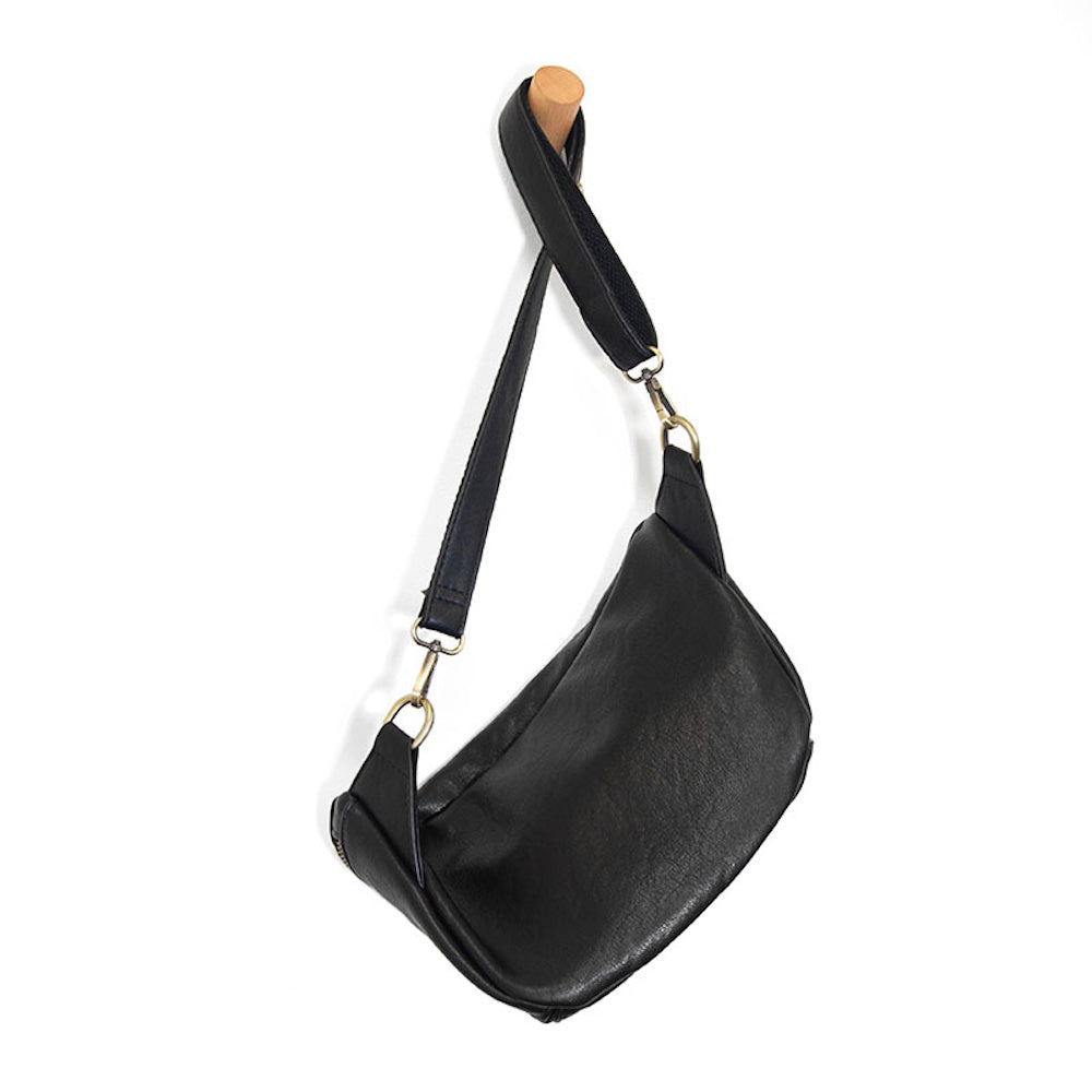 Small black leather hobo sling bag with brass hardware hanging on a wall hook, minimalist style.