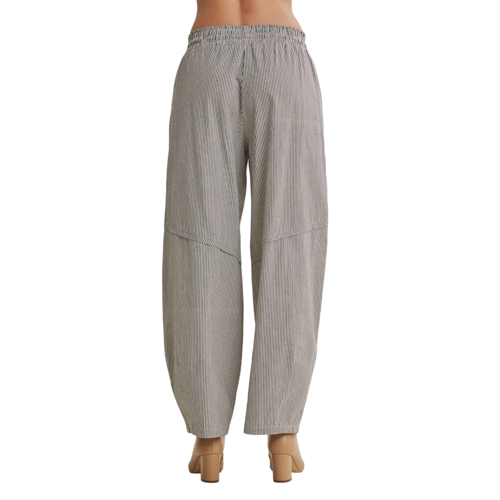 Back view of model wearing black and white fine-striped relaxed barrel pants with an elastic waist.