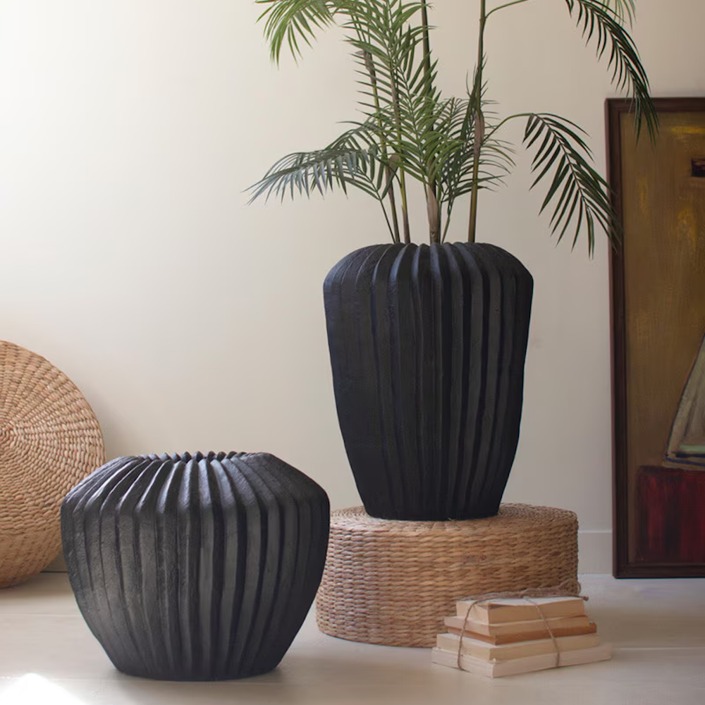 Two black fluted stone composite urns styled with a palm plant, woven textures, and books in a modern interior.
