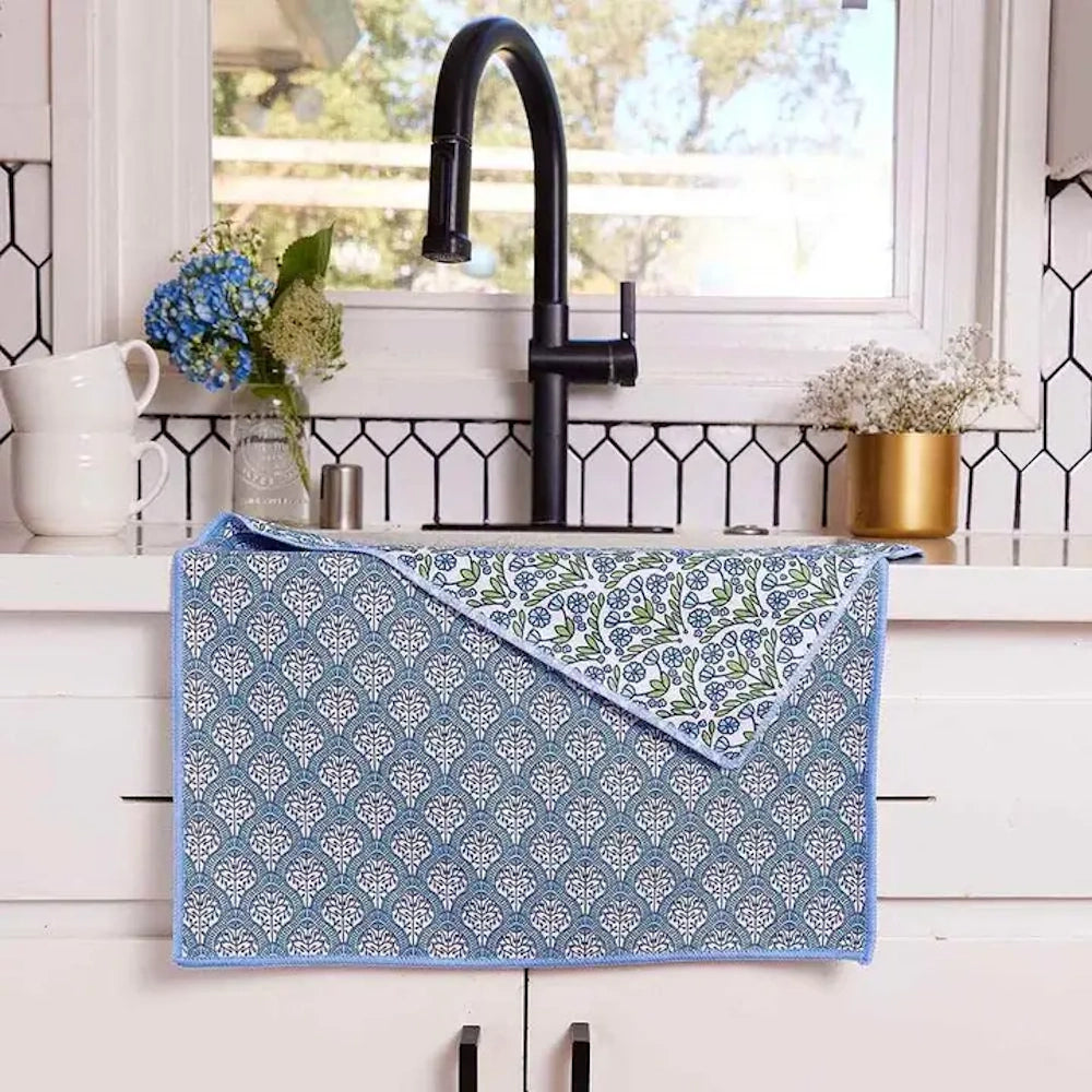 Absorbent blue patterned microfiber dish mat with floral reversible side, hanging on white kitchen counter and cabinet drawer.