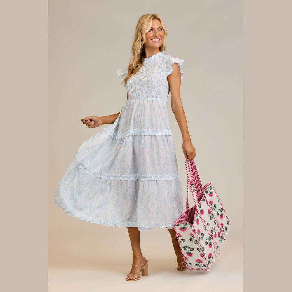 Woman in a light blue tiered floral dress holding a pink block-print tote bag against a neutral background.