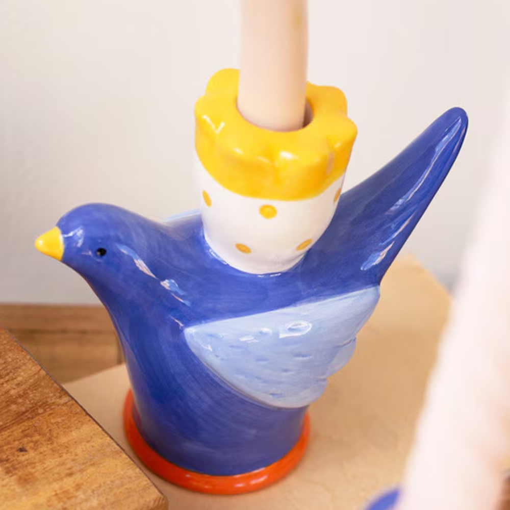Hand-painted blue ceramic bird taper candle holder with yellow polka dot details and a cream candle.