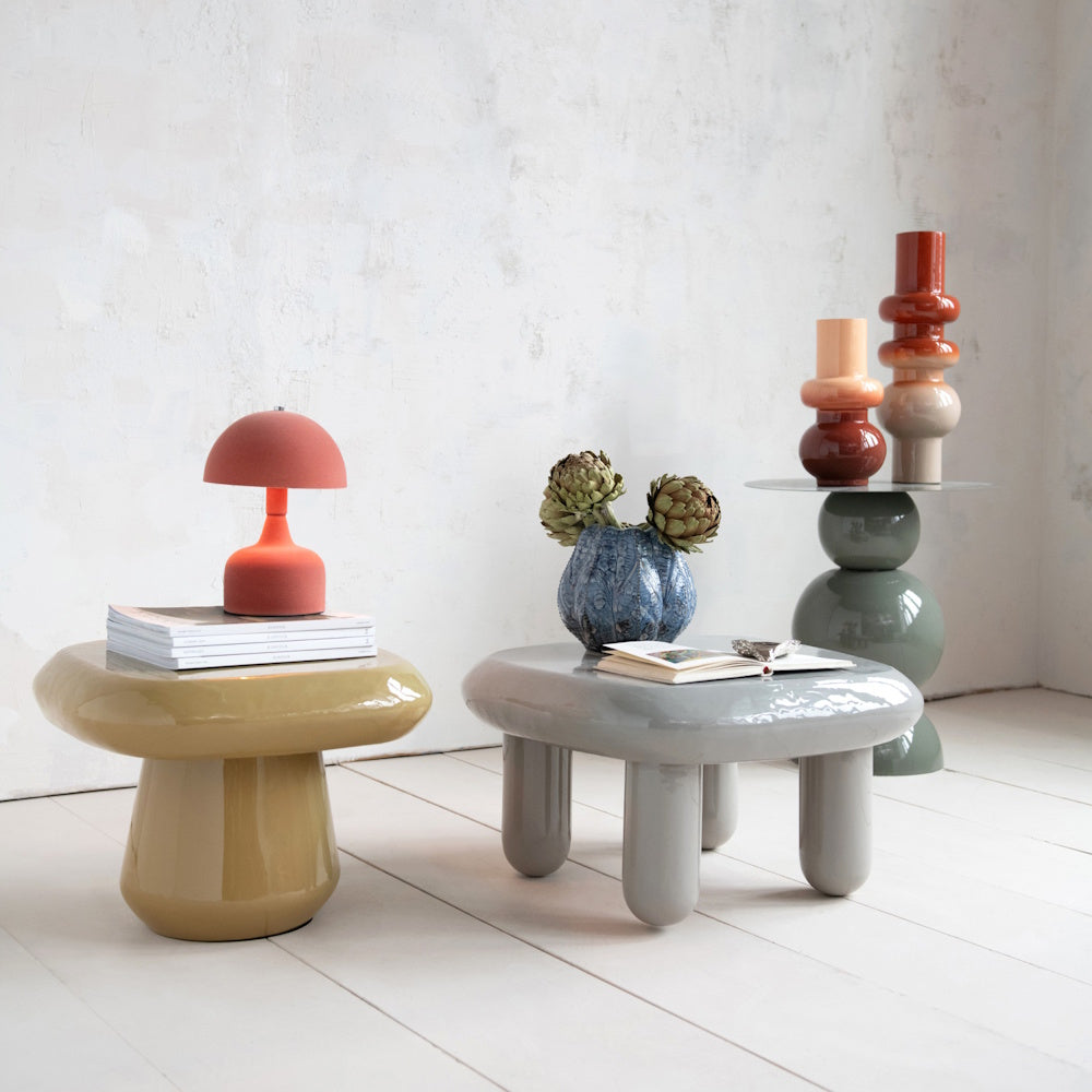 Modern ceramic tables with an orange lamp, a blue textured vase with artichokes, and stacked decor.