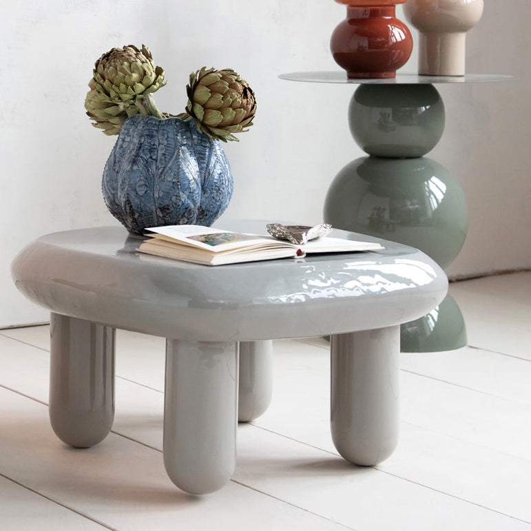 Blue textured vase with artichokes on a glossy grey coffee table beside a modern side table.