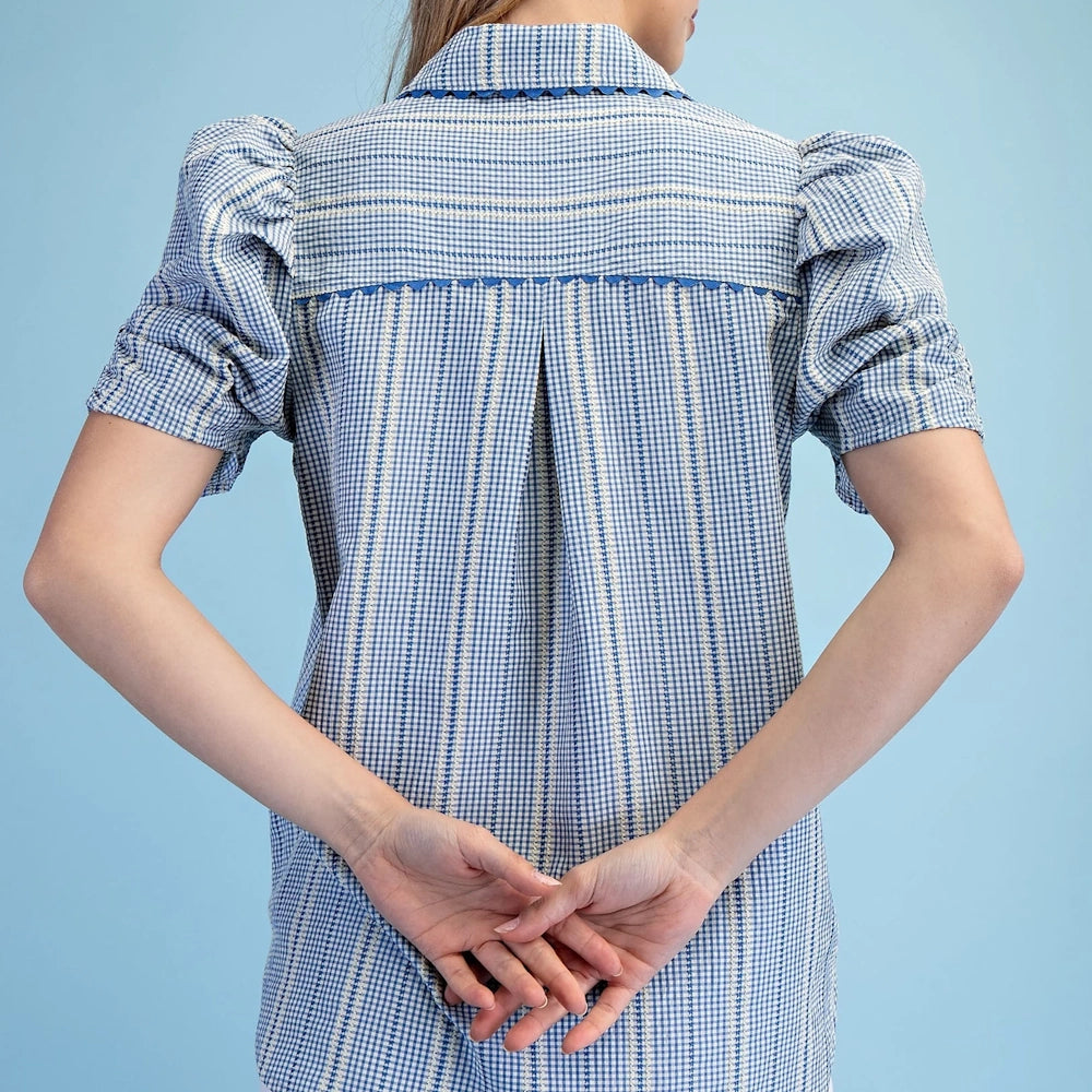 Back view of a blue embroidered gingham button-down shirt with ric-rac trim, puffed gathered sleeves, and an inverted pleat.