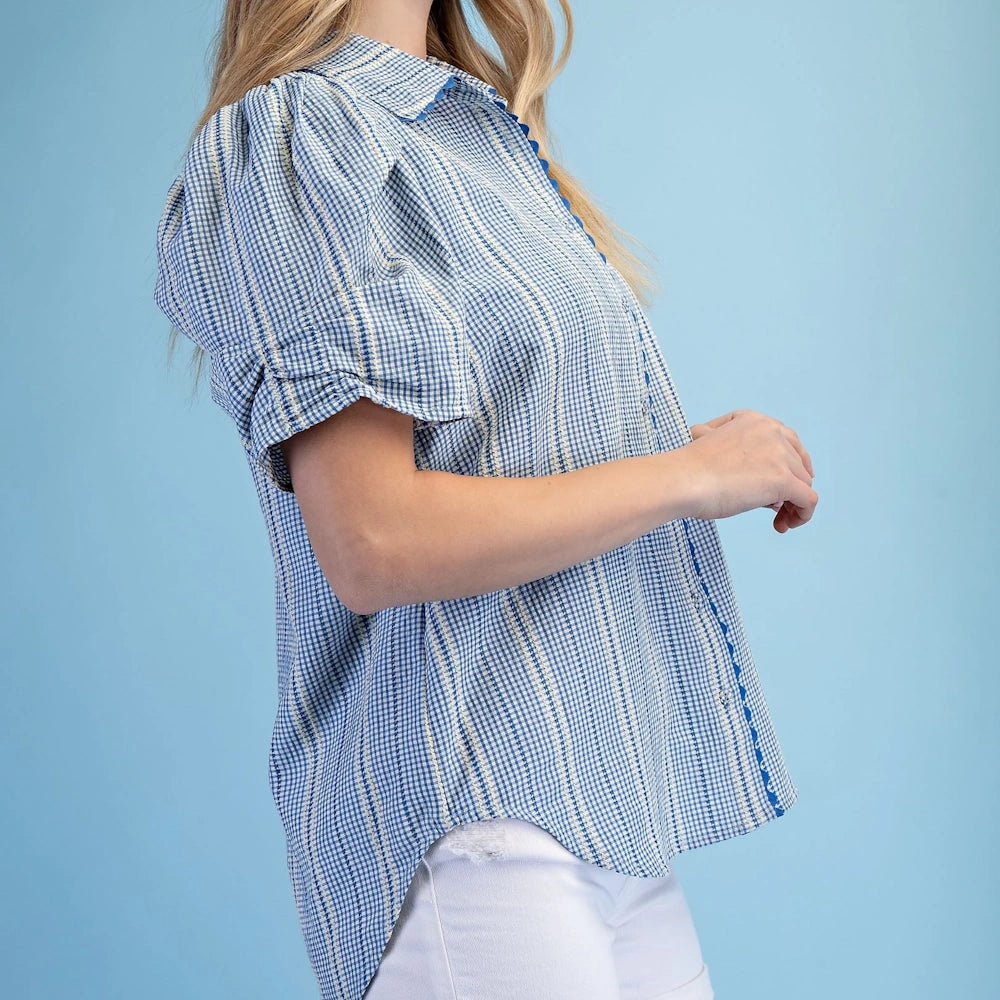 Side view of a blue gingham embroidered button-down top with puffed gathered sleeves and blue ric-rac trim.