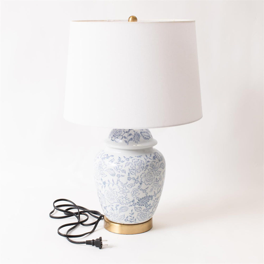 Blue and white floral ginger jar table lamp with white drum shade and brass base on a white background.