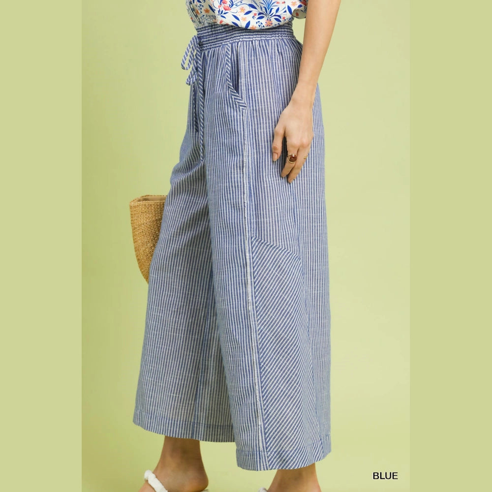 Blue and white vertical striped wide-leg linen pants with drawstring waist and side pockets against a green background.