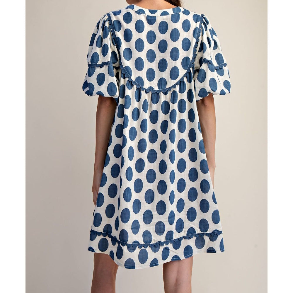 Back view of a white mini dress with blue polka dots, puff sleeves, and scalloped trim details.