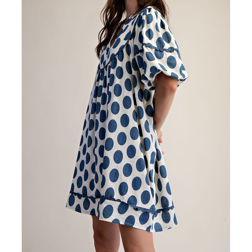 Side view of a white linen mini dress with large blue polka dots and puffed short sleeves.