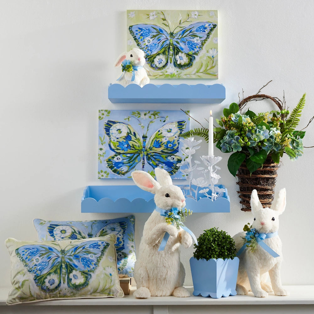 Blue scalloped shelves and white bunnies with butterfly art and pillows in a spring-themed blue and green display.
