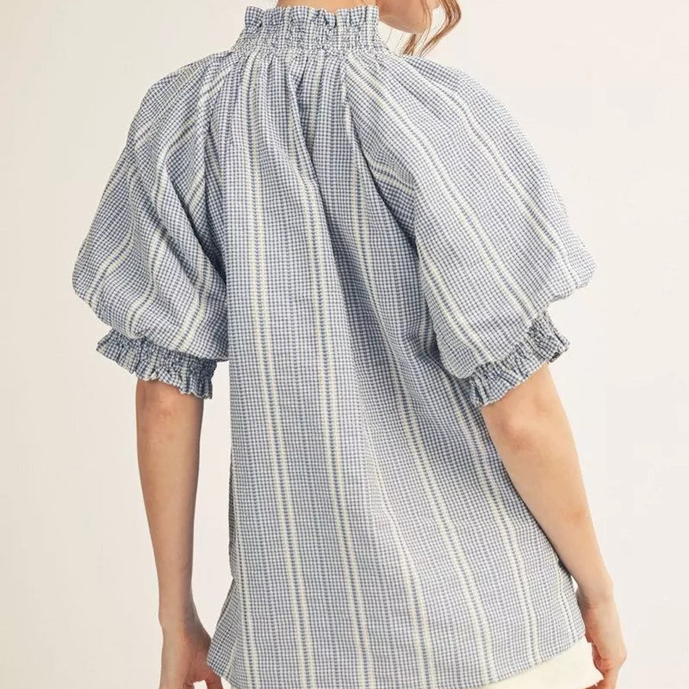 Back view of a blue and white gingham smocked-neck blouse with puffed sleeves and vertical stripes.
