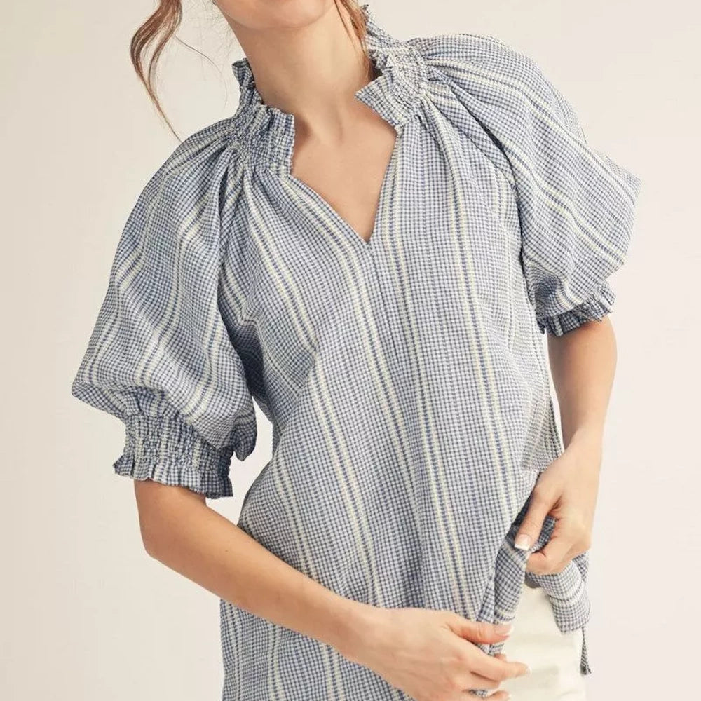 Woman wearing a blue and white gingham blouse with puffed sleeves and a ruffled neckline.
