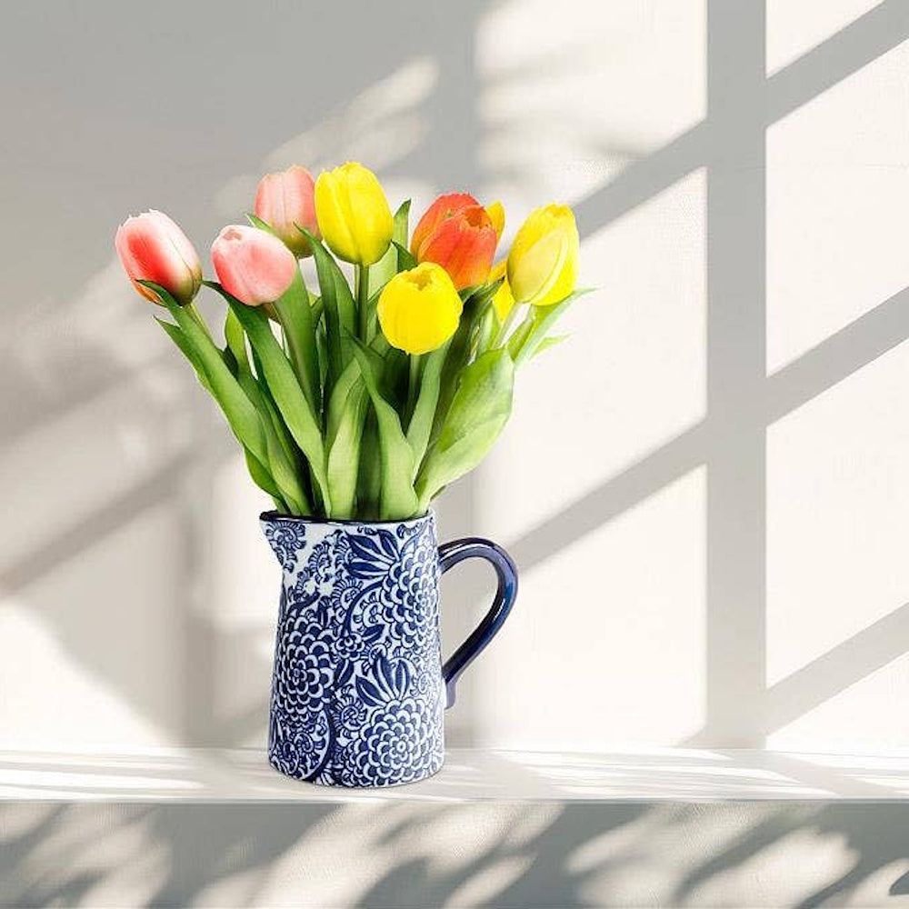 Tulips in a blue and white floral ceramic pitcher on a sunlit ledge.