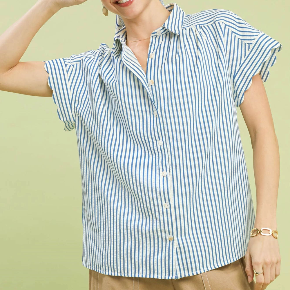 Woman wearing a blue and white striped button-down top with scalloped short sleeves and tan trousers.