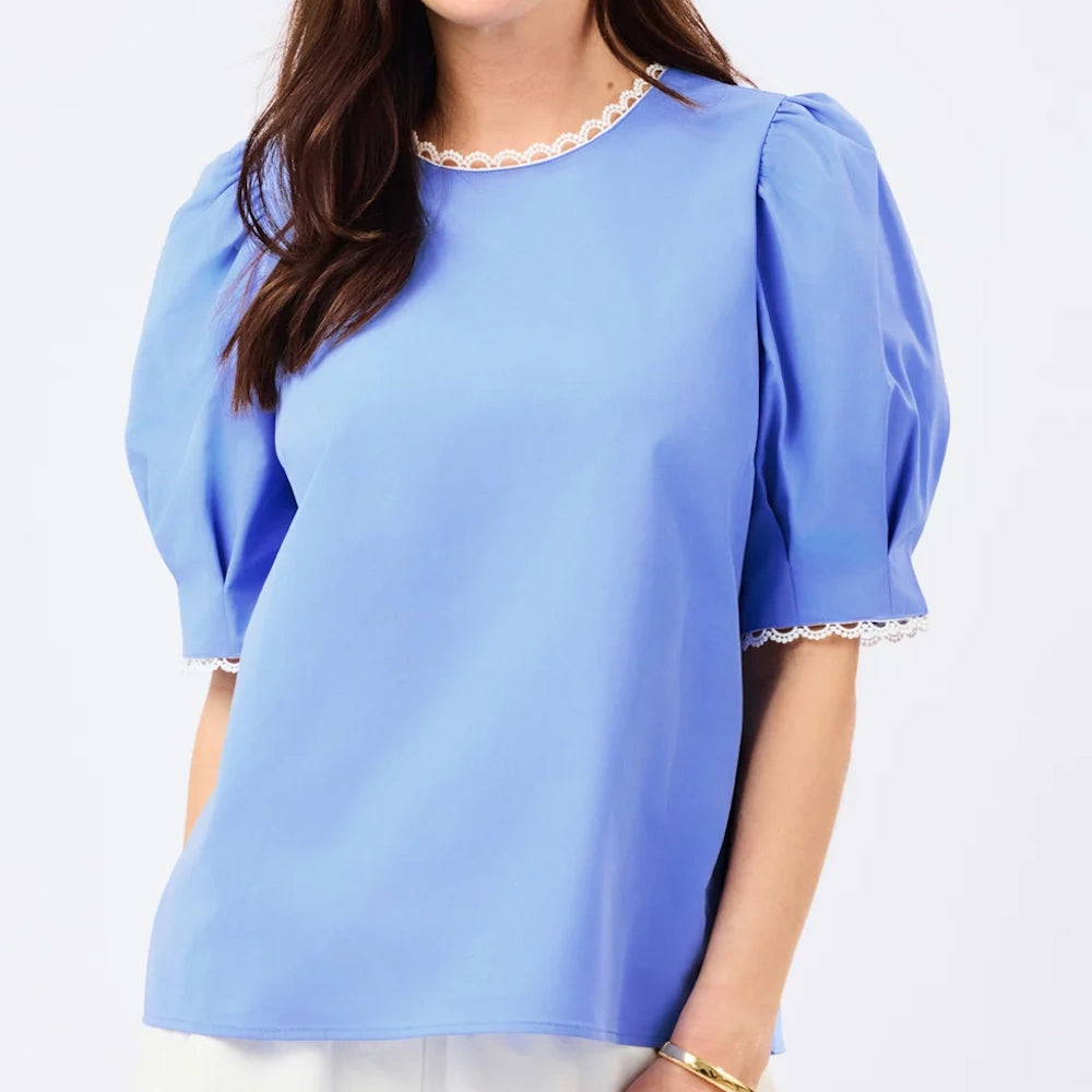 A woman wearing a light blue short-sleeved top with puff sleeves and white lace trim along the collar and cuffs.
