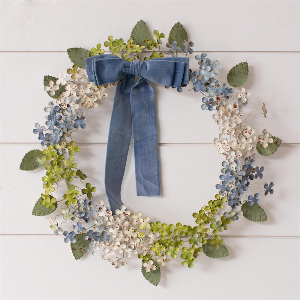 Rustic metal floral wreath with blue velvet bow on a white shiplap wall.