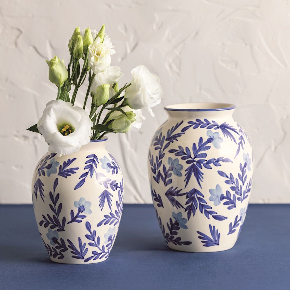 Two white ceramic vases with blue vine and flower patterns; one holds white lisianthus flowers.