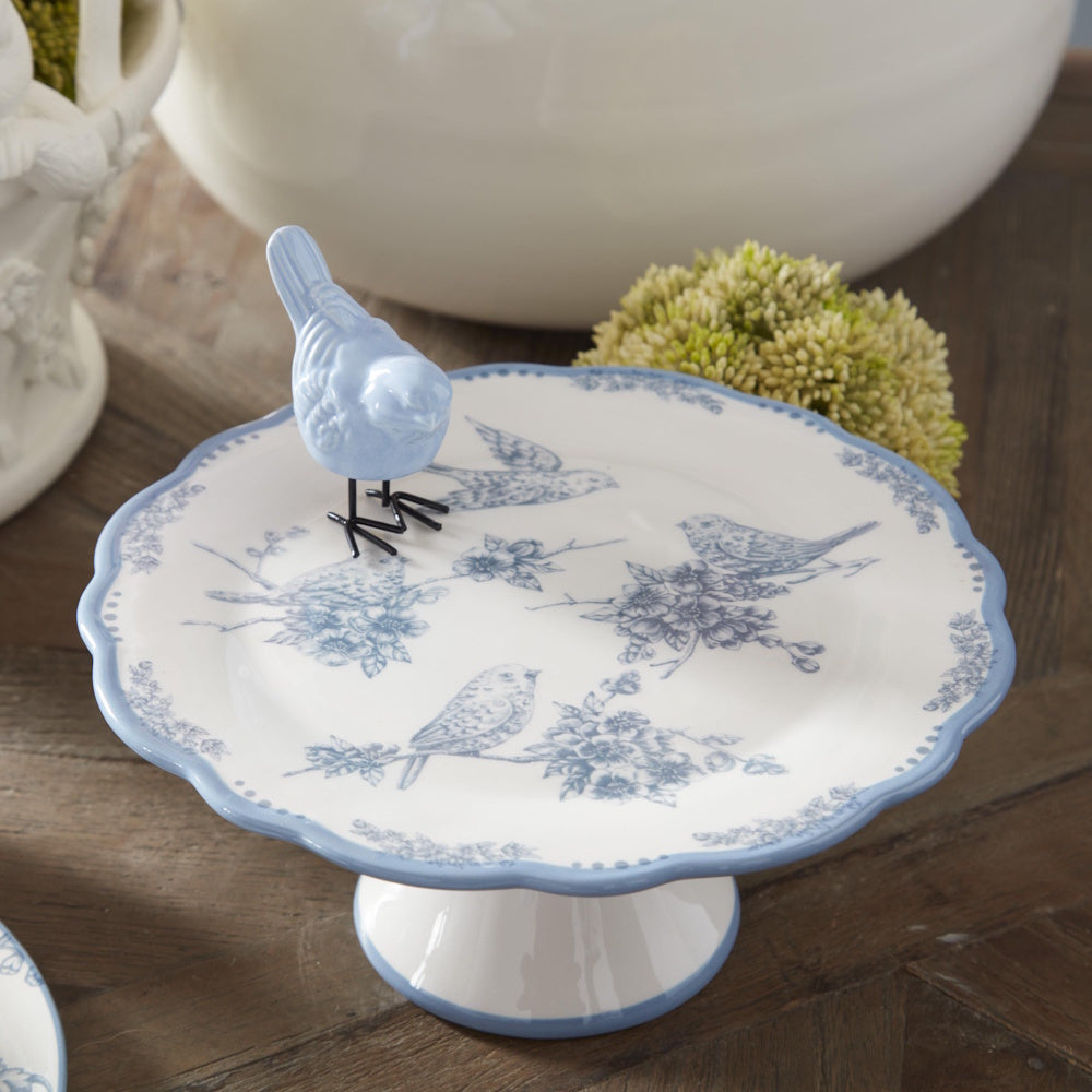 White and blue bird-themed ceramic cake stand featuring floral bird patterns and a small blue bird figurine.
