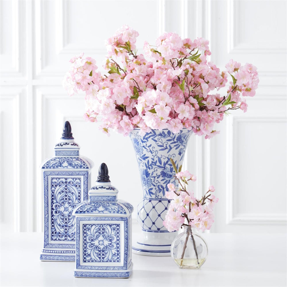 Blue and white chinoiserie fluted vase with pink cherry blossoms and matching ginger jars on a white table.