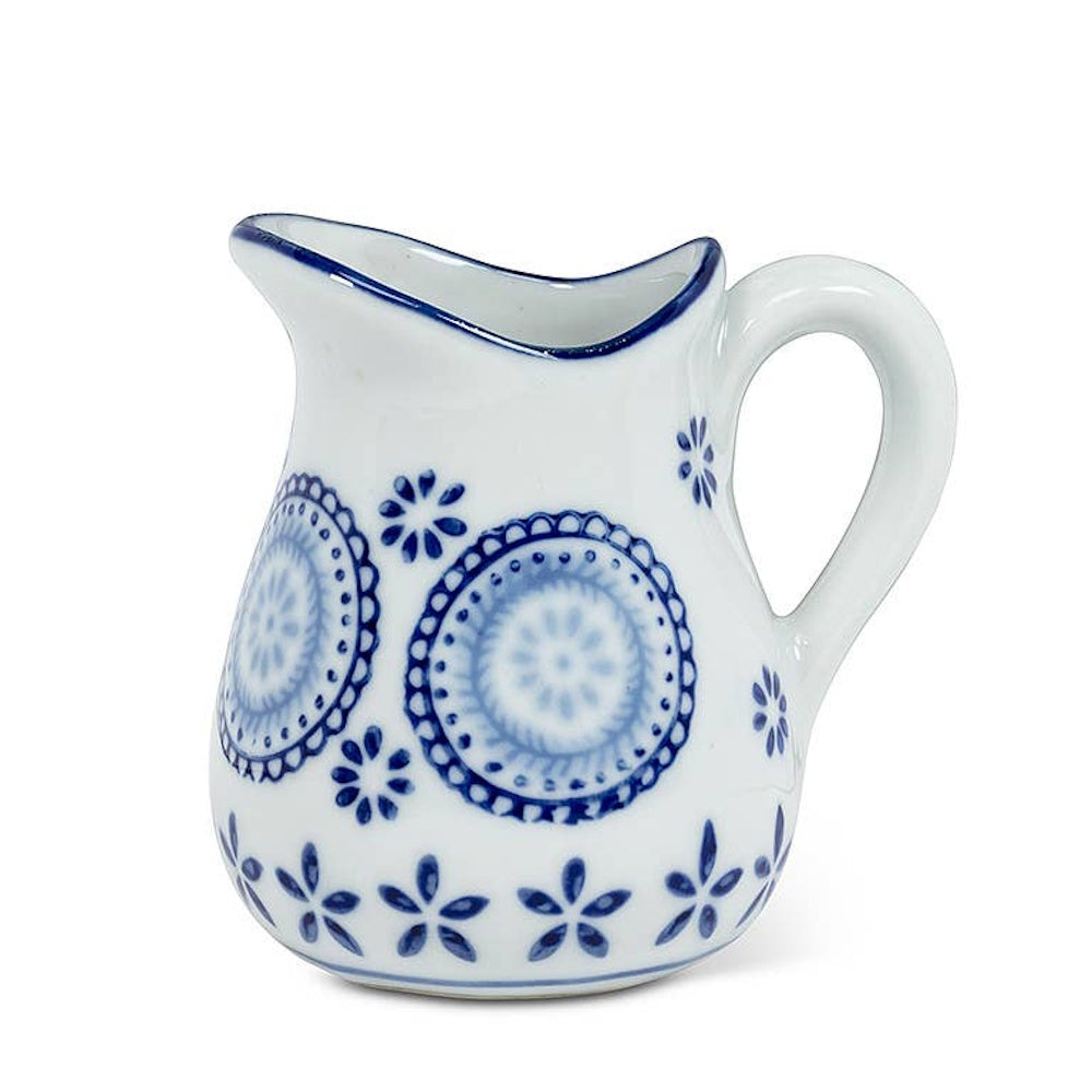 Small white ceramic pitcher with painted blue floral and circular patterns against a plain background.