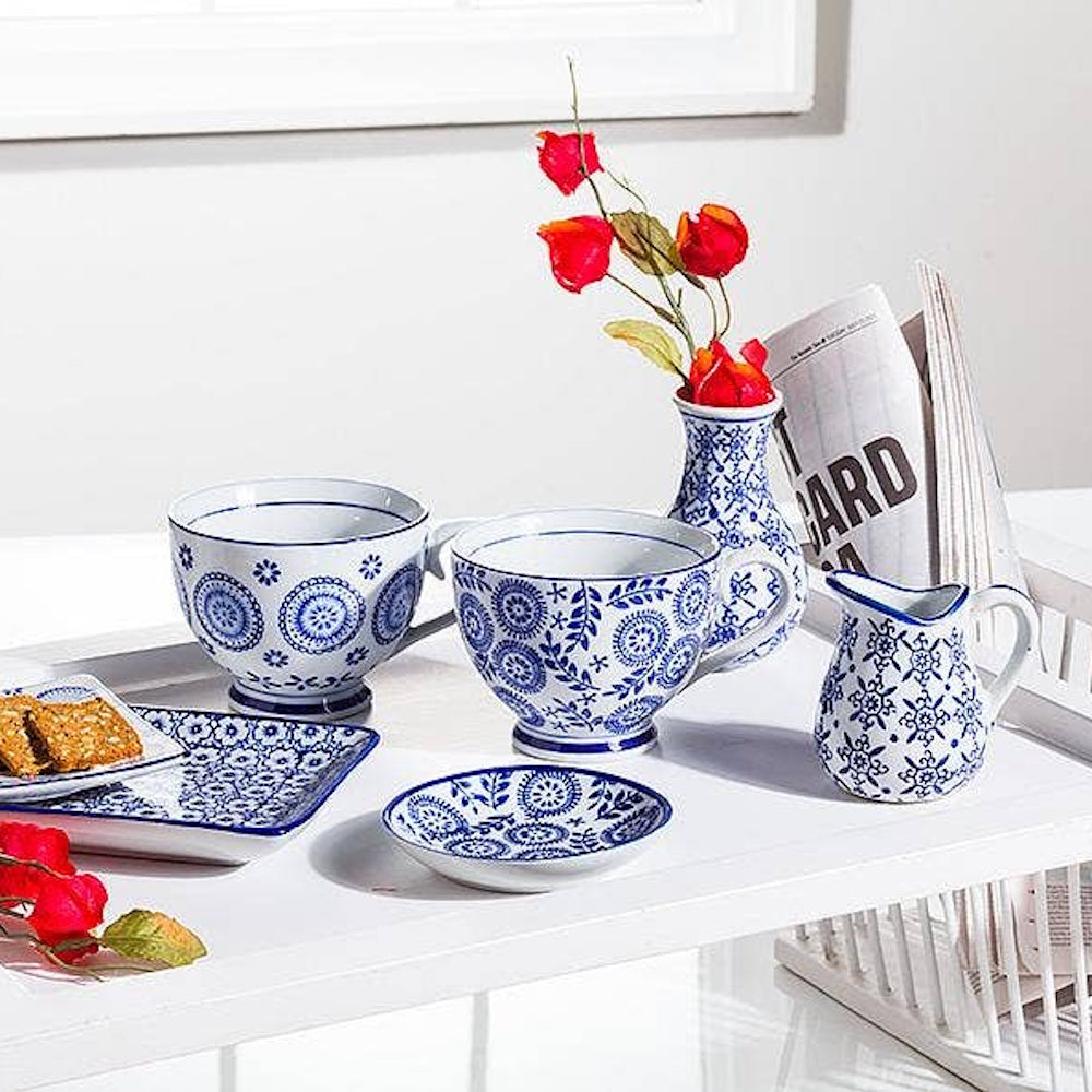 Blue and white patterned ceramic tea set with cups, small pitcher, plates, and a vase on a serving tray.