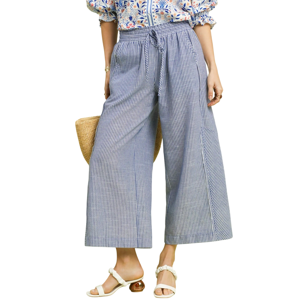 Blue and white striped wide-leg linen pants with a drawstring waist, paired with white sandals and a straw bag.