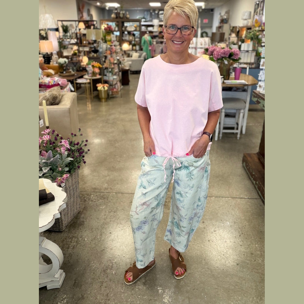 Woman in a pink t-shirt and floral barrel jeans standing in a boutique, holding her hands in her pockets.