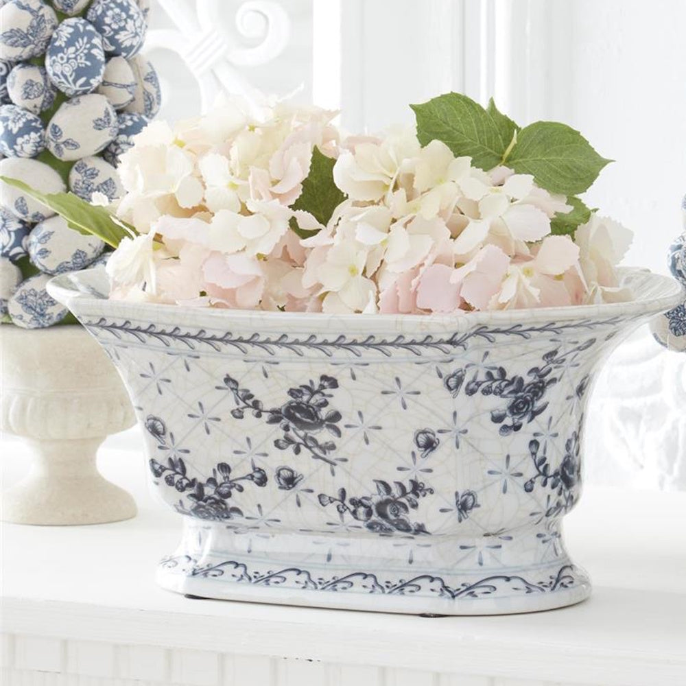 Pale pink hydrangeas in a blue and white Chinoiserie floral ceramic planter bowl on a white mantel.