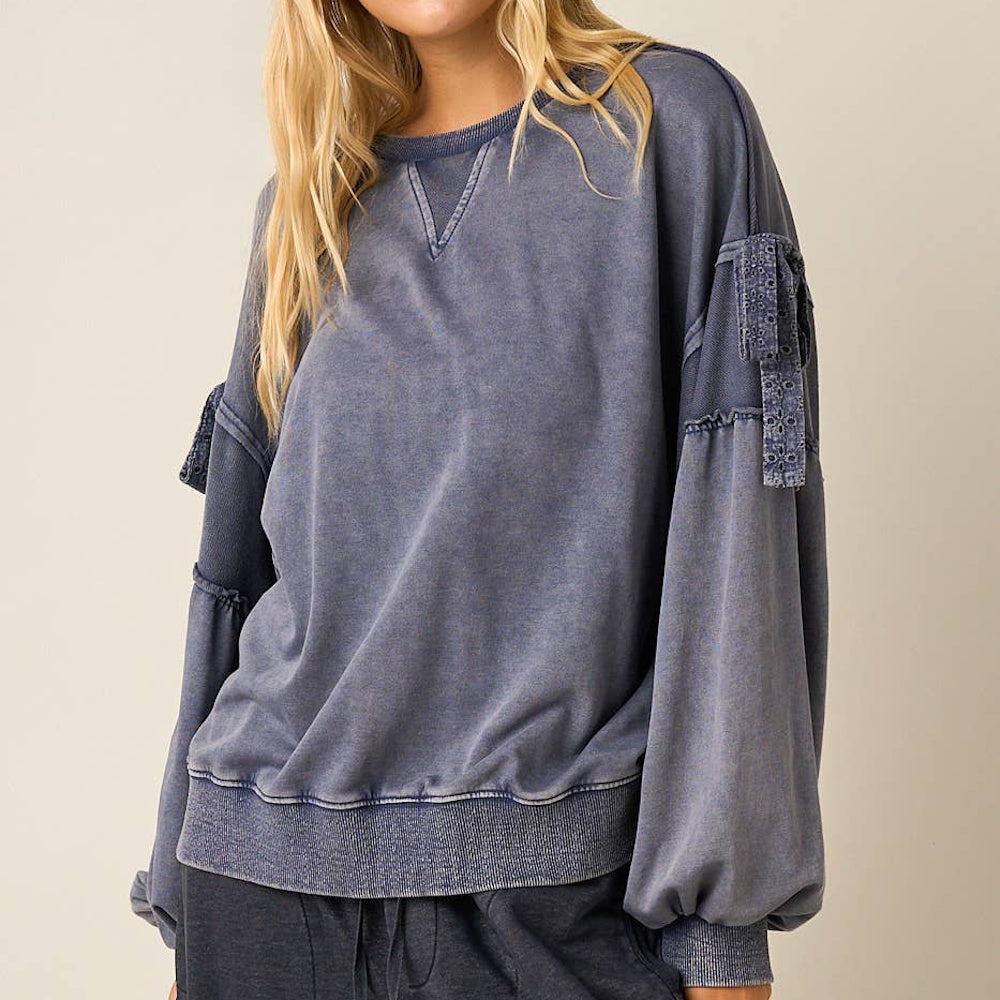 Front-angled view of a blue mineral washed cotton sweatshirt with long balloon sleeves and bow accents.