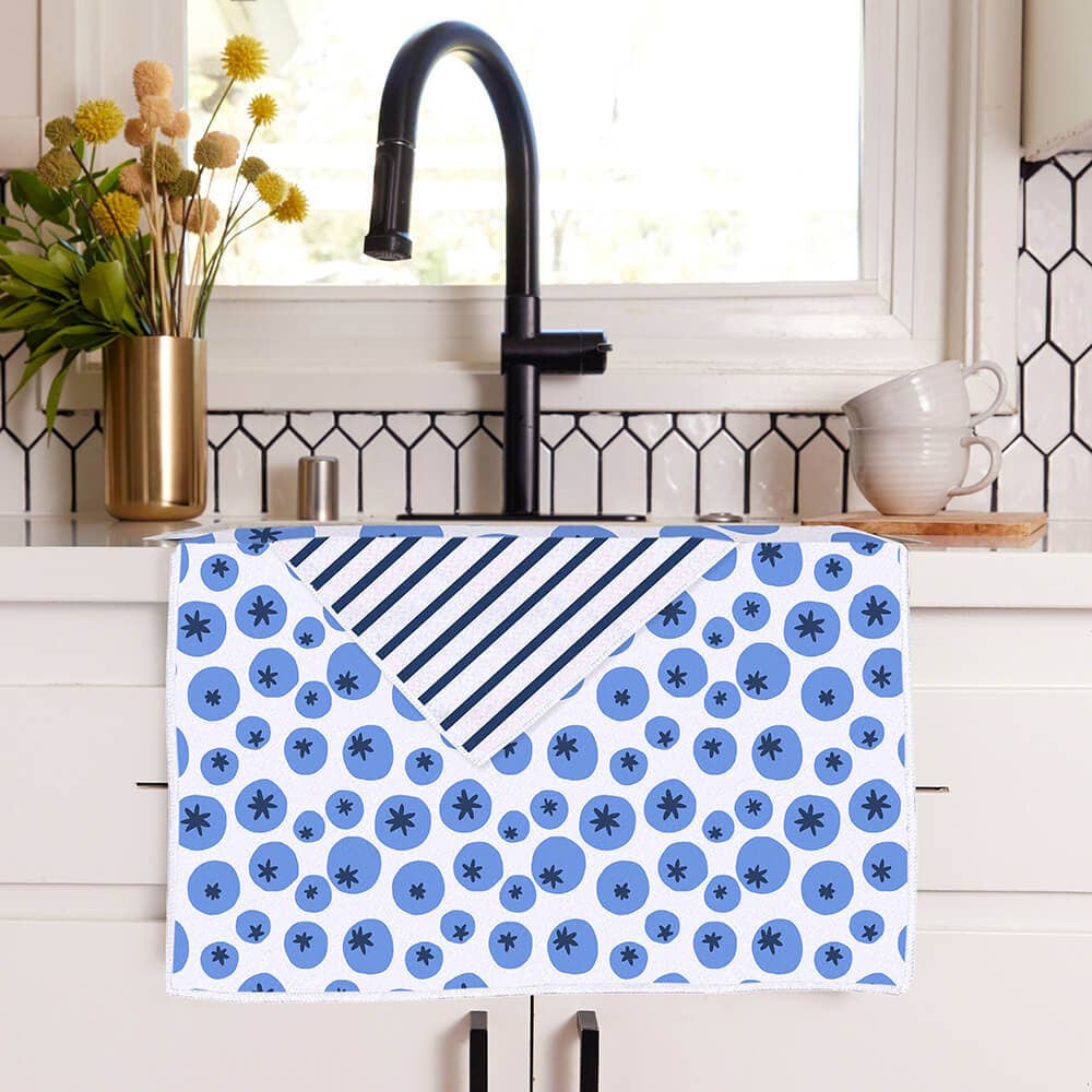 Blueberry pattern kitchen towel with striped reverse side hanging over a sink counter.