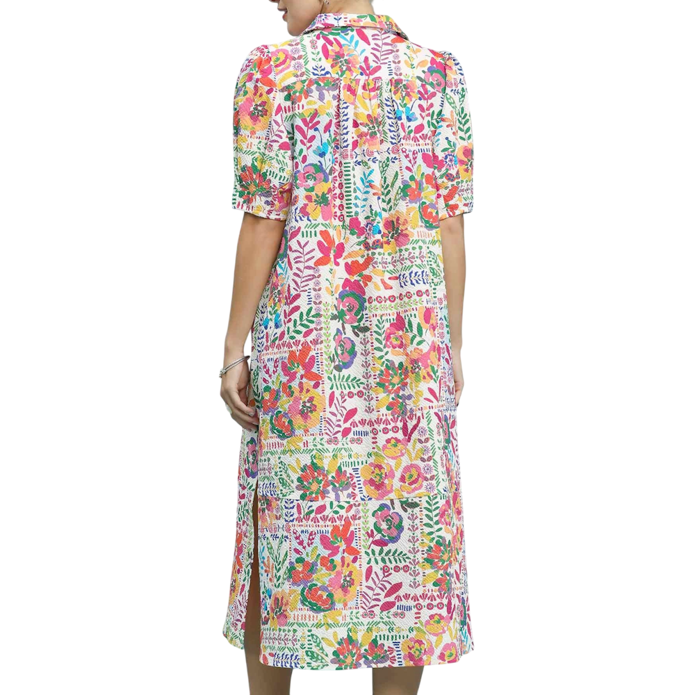 Back view of a woman wearing a colorful, floral patchwork midi dress with short sleeves and a side slit.