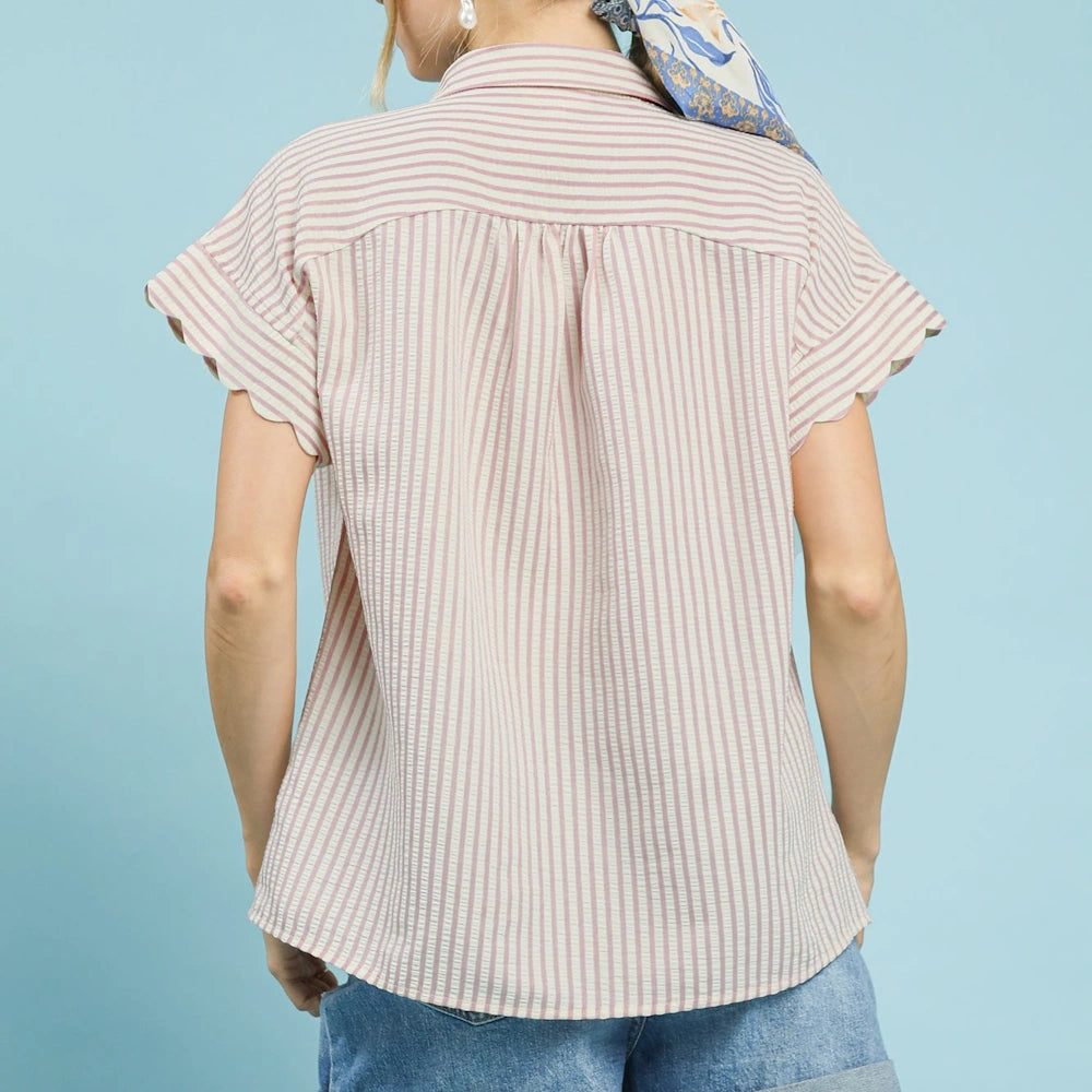 Back view of a woman wearing a blush pink and white striped button-down shirt with scalloped short sleeves and blue denim.