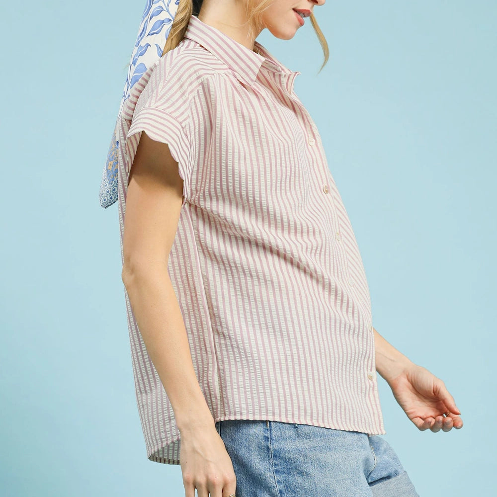 Blush and white striped button-down shirt with scalloped short sleeves paired with denim jeans against a blue background.