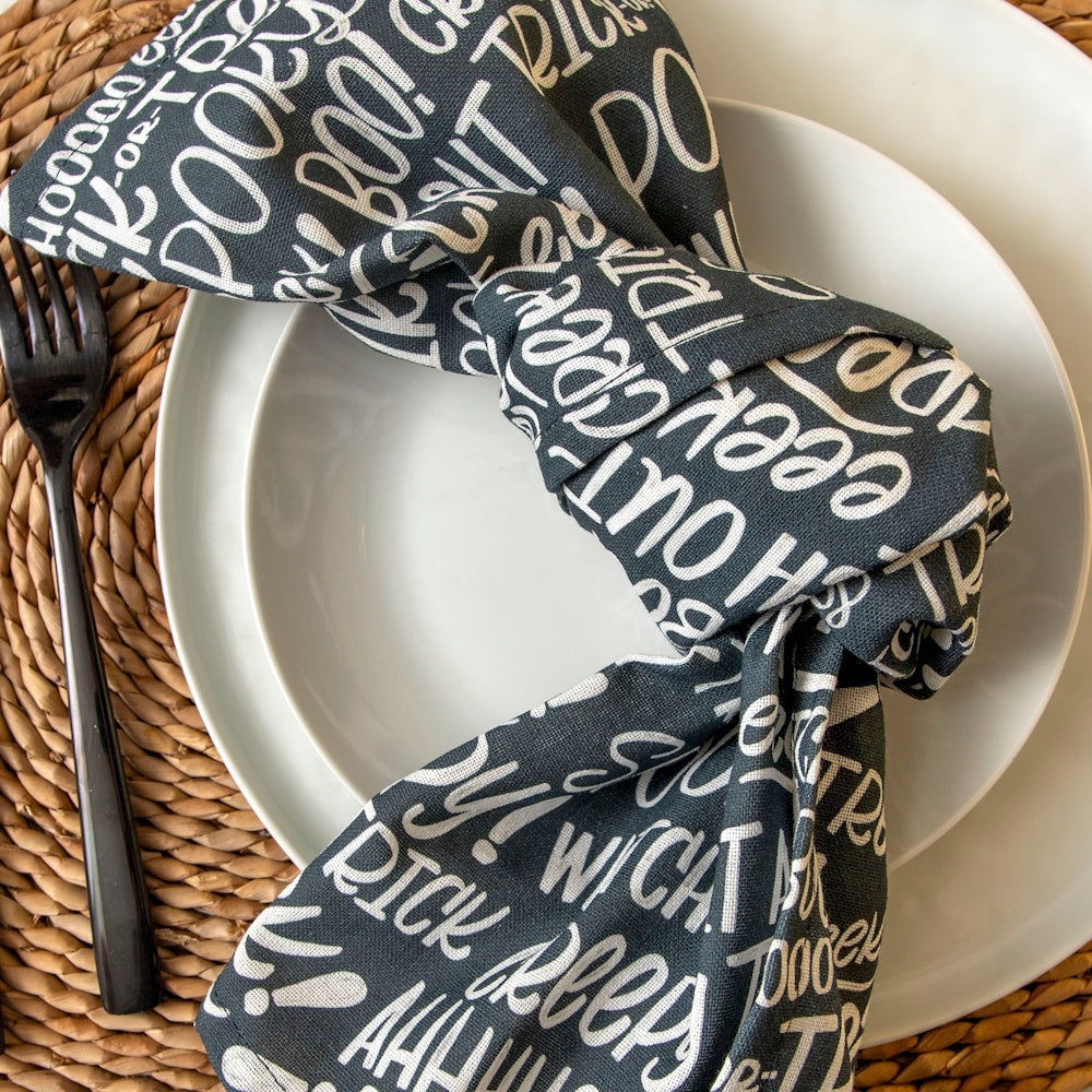 Black and white Halloween towel tied in a knot on a white plate with a black fork and woven placemat.