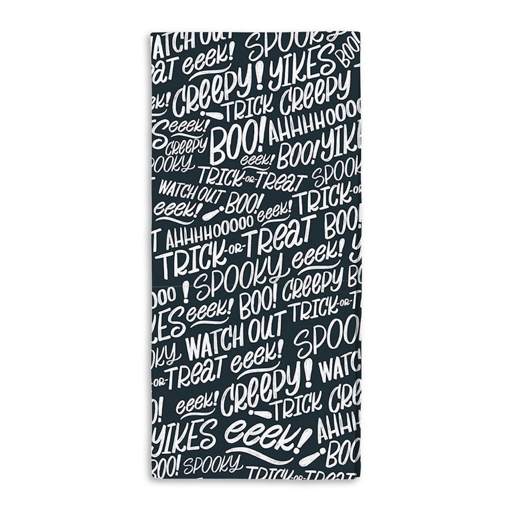 Black kitchen towel covered in white hand-lettered Halloween phrases like BOO, spooky, and trick-or-treat.