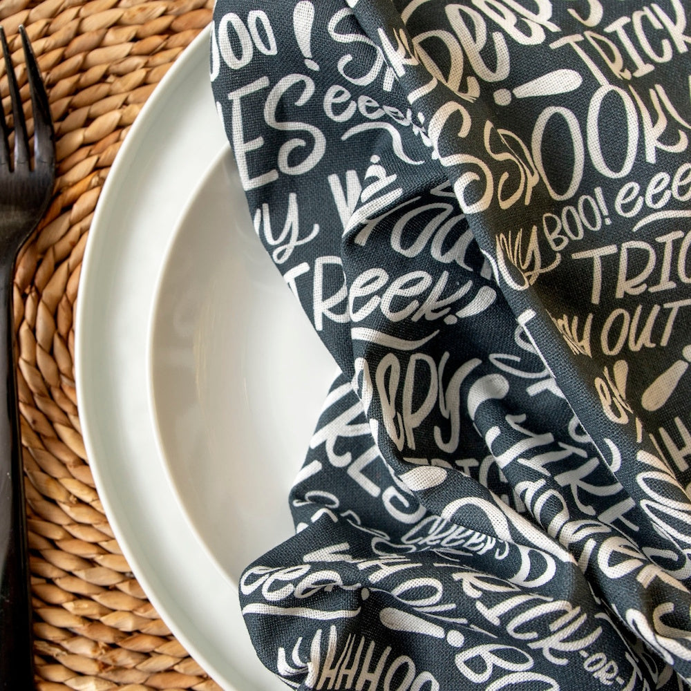 A black Halloween towel with white text like "BOO!" and "SPOOKY" draped on a white plate.